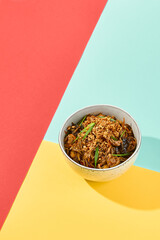 Asian fried buckwheat noodles with chicken on coloured background Fried noodles in ceramic bowl on yellow, red and blue background. Stir-fry soba in trendy style with shadows. Vibrant food
