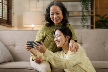 Asian mature woman hugging with daughter while sitting on sofa, mother day concept.