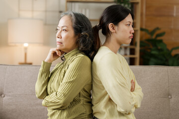 Asian mature mom and adult daughter have fight at home while sitting on sofa.