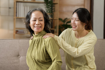 Asian daughter giving an elderly mother a relaxing massage while sitting on the sofa