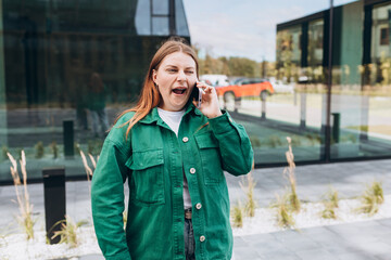 Fototapeta premium Beautiful Bored redhead woman talking with her smartphone. Woman yawning and using smartphone on city street.