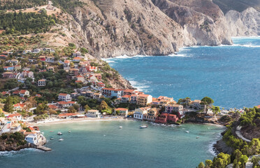 Fototapeta premium Picturesque aerial shot of colorful fishing Asos village houses on Cephalonia island, Greece. Steep cliff banks washed by blue Ionian Sea waves.