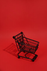 Black shopping cart with shadow on red background, copy space