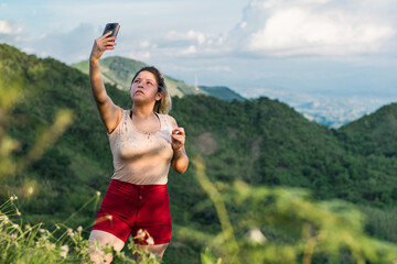 beautiful young latina woman, on top of a mountain taking a picture of herself. girl on a trip in...