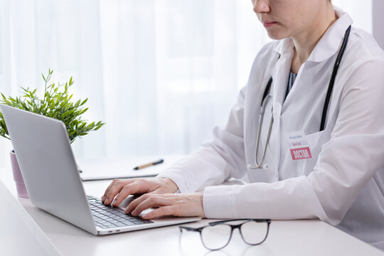 A female doctor works at a laptop in a hospital office. Doctor records data in a portable device, medical office, hospital work, medical worker, glasses, stethoscope. High quality photo