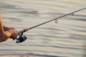 telescopic fishing rod with inertia reel in men's hands on the background of river water