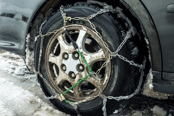 Close-up of a car wheel with snow chains. Dirty rims. Rubber in the snow. Car wheel with chains. Safety on winter snowy roads.