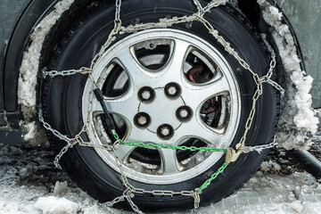 A car wheel wrapped with chains. Close-up. In the fenders of the car muddy snow. Snow chains on the...