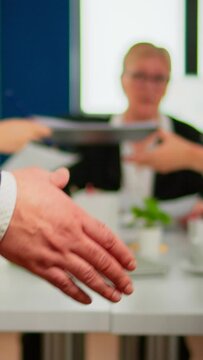 Close up of multiracial business partners standing in front of conference desk shaking hands after signing partnership contract. Diverse team being happy for successful negotiations in startup company