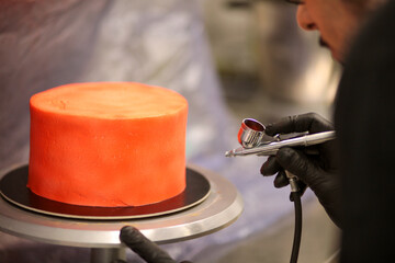 pastry chef designer using edible red paint airbrush to spray frosted cup cake