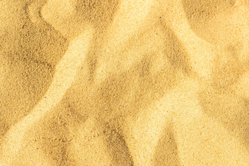 Close-up of a sandy beach. Background with sand unevenly swept away by wind and waves into small dunes. Background for a cover or design on the theme of travel.