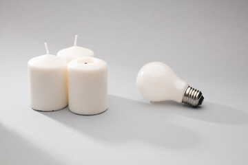 concept lack of electricity supply. three white candles and light bulb on gray background