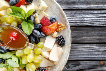 Cheese platter: variety of cheeses on wooden plate with fruits, nuts and berries Horizontal photo