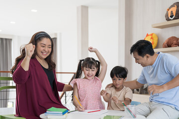 Happy asian family reading a book together at home. Smiling parents and teen daughter and son spending time together.