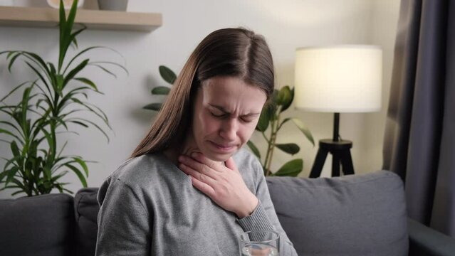 Close up of unhealthy young woman have sore throat cough symptom and feel sick from virus or bacteria infection influenza by touching neck and hard to swallow and drink water, experience loss of voice