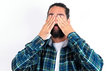 young bearded hispanic man wearing plaid shirt over white background covering eyes with both hands, doesn't want to see anything or feeling ashamed. Human feelings reactions.