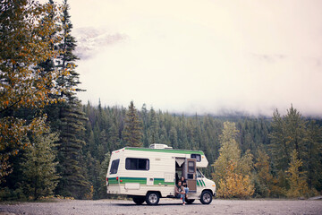 Couple sitting in camper van on dirt road by trees