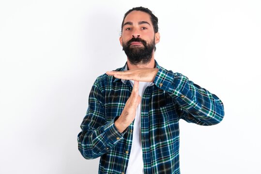 young bearded hispanic man wearing plaid shirt over white background feels tired and bored, making a timeout gesture, needs to stop because of work stress, time concept.