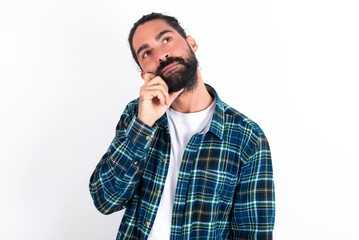 Fototapeta premium Face expressions and emotions. Thoughtful young bearded hispanic man wearing plaid shirt over white background holding hand under his head, having doubtful look.