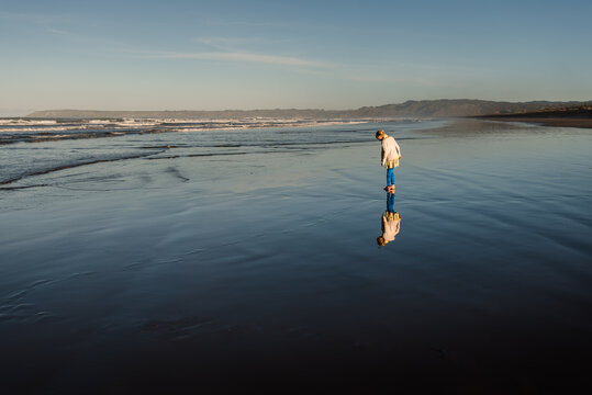 Girl standing in shallow water at beach with reflection