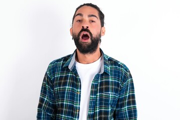 Emotional attractive young bearded hispanic man wearing plaid shirt over white with opened mouth...