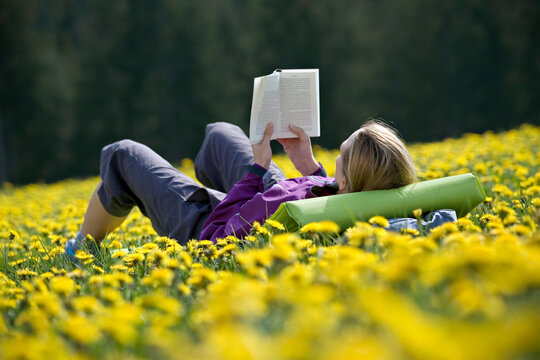 A woman reads in a field of flowers.