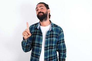 Naklejka premium No sign gesture. Closeup portrait unhappy young bearded hispanic man wearing plaid shirt over white background raising fore finger up saying no. Negative emotions facial expressions, feelings.