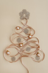 Top view of baubles balls, stars and ribbons arranged in Christmas tree with toys on pastel beige background