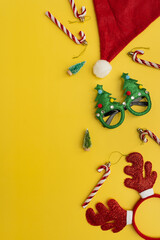 Funny New Year, Christmas accessories for winter holidays party celebration on yellow background. Christmas eyeglasses, candy canes, deer horns, Santa hat, toy trees
