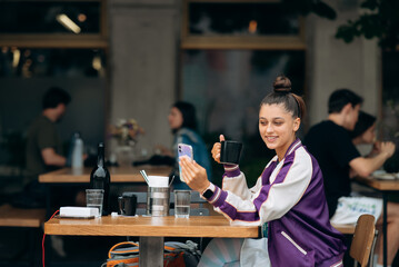 Young woman sitting outdoors cafe and drinking coffee holding smartphone