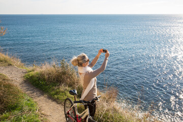 Woman with bike takes photo above the sea