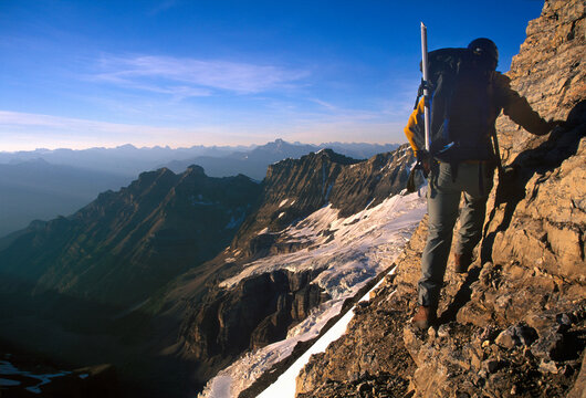 Mountaineer walking along narrow ledge above valley and mountains