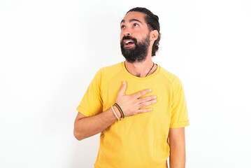 Joyful young bearded hispanic man wearing yellow T-shirt over white background expresses positive...