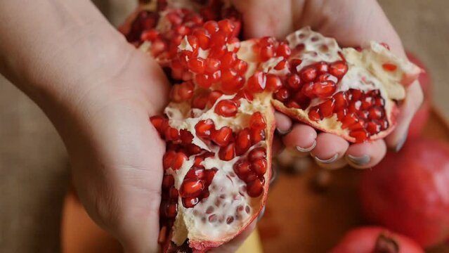 Women's hands break in half a ripe red pomegranate with a red seed inside. Close-up of a ripe pomegranate is broken by a woman. Healthy fruit is rich in vitamins