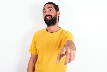 Obraz premium Excited positive young bearded hispanic man wearing yellow T-shirt over white background points index finger directly at you, sees something very funny. Wow, amazing
