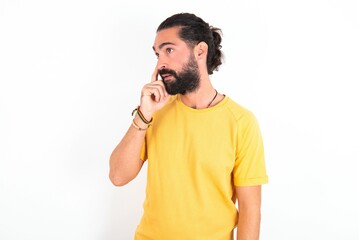 Astonished young bearded hispanic man wearing yellow T-shirt over white background looks aside surprisingly with opened mouth.