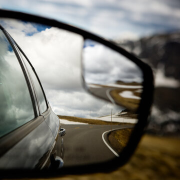 Mountain Road And Cloudy Sky From A Cars View Mirror.