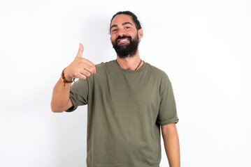 Fototapeta premium young bearded hispanic man wearing green T-shirt over white background doing happy thumbs up gesture with hand. Approving expression looking at the camera showing success.