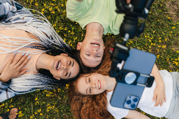 Portrait of a group of friends lying on the grass in the park, smiling and making selfie. Top view....