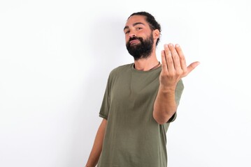 young bearded hispanic man wearing green T-shirt over white background inviting to come with hand. Happy that you came