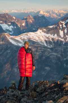 Portrait Of A Male Climber Wearing A Sleeping Bag To Stay Warm On The Summit Of A Joffre Peak