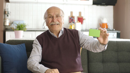 Old man showing green box and imaginary product on sofa, smiling. Creative 3d artists can replace...