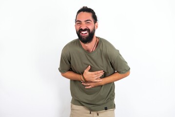 young bearded hispanic man wearing green T-shirt over white background smiling and laughing hard out loud because funny crazy joke with hands on body.