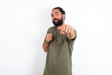 Fototapeta premium young bearded hispanic man wearing green T-shirt over white background Punching fist to fight, aggressive and angry attack, threat and violence