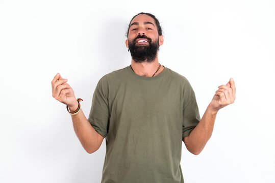 young bearded hispanic man wearing green T-shirt over white background doing money gesture with hands, asking for salary payment, millionaire business