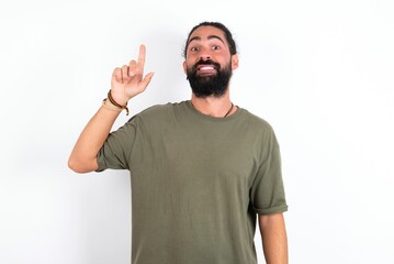 young bearded hispanic man wearing green t-shirt over white background showing and pointing up with finger number one while smiling confident and happy.