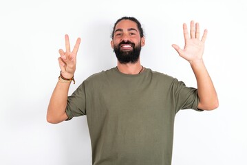 Naklejka premium young bearded hispanic man wearing green t-shirt over white background showing and pointing up with fingers number seven while smiling confident and happy.