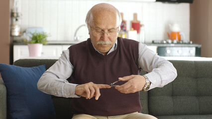 An elderly man sitting in his armchair at home is cutting his nails with nail clippers. Personal...