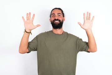 Naklejka premium young bearded hispanic man wearing green t-shirt over white background showing and pointing up with fingers number ten while smiling confident and happy.
