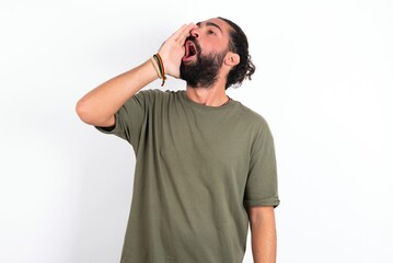 young bearded hispanic man wearing green t-shirt over white background shouting and screaming loud to side with hand on mouth. Communication concept.